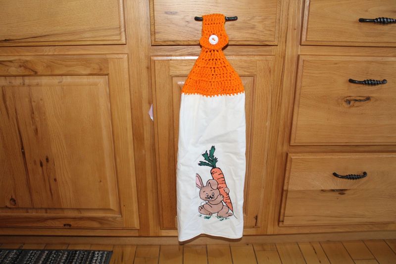 Hand painted bunny kitchen towel with carrot and orange crochet topper hanging on cabinet handle.