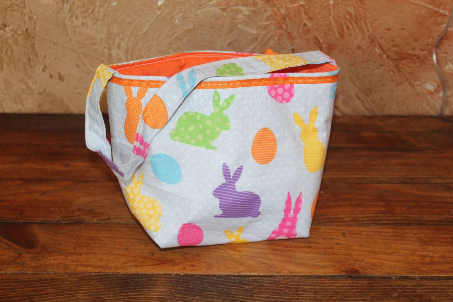 Handmade Easter basket tote with colorful bunny and egg print and bright orange lining for kids Easter egg hunts.