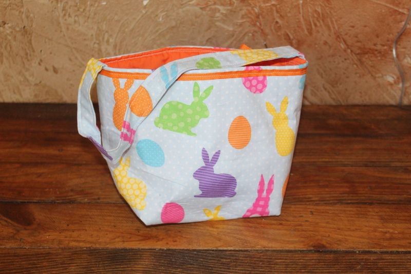 Handmade Easter basket tote with colorful bunny and egg print and bright orange lining for kids Easter egg hunts.