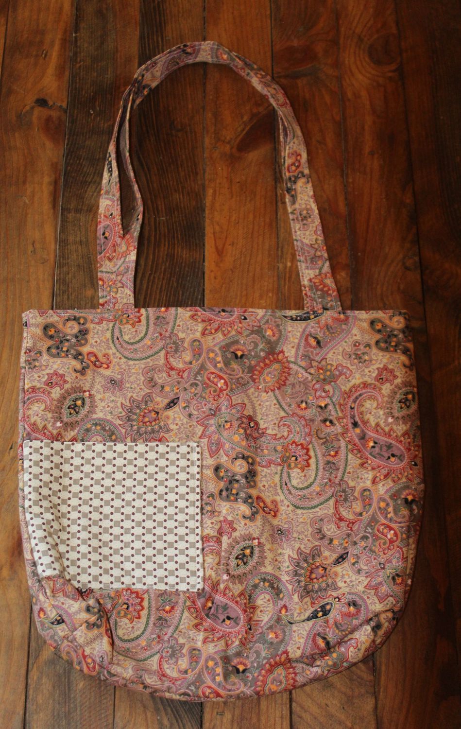 Handmade paisley cotton tote bag with front pocket on wooden background.