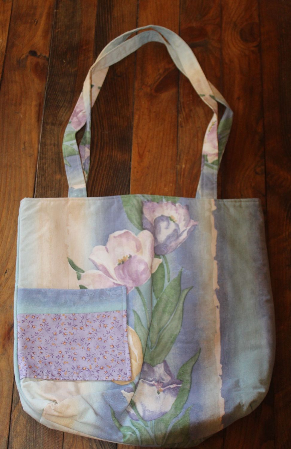 Handmade floral tote bag with front pocket on wooden background – reusable fabric shopping bag.