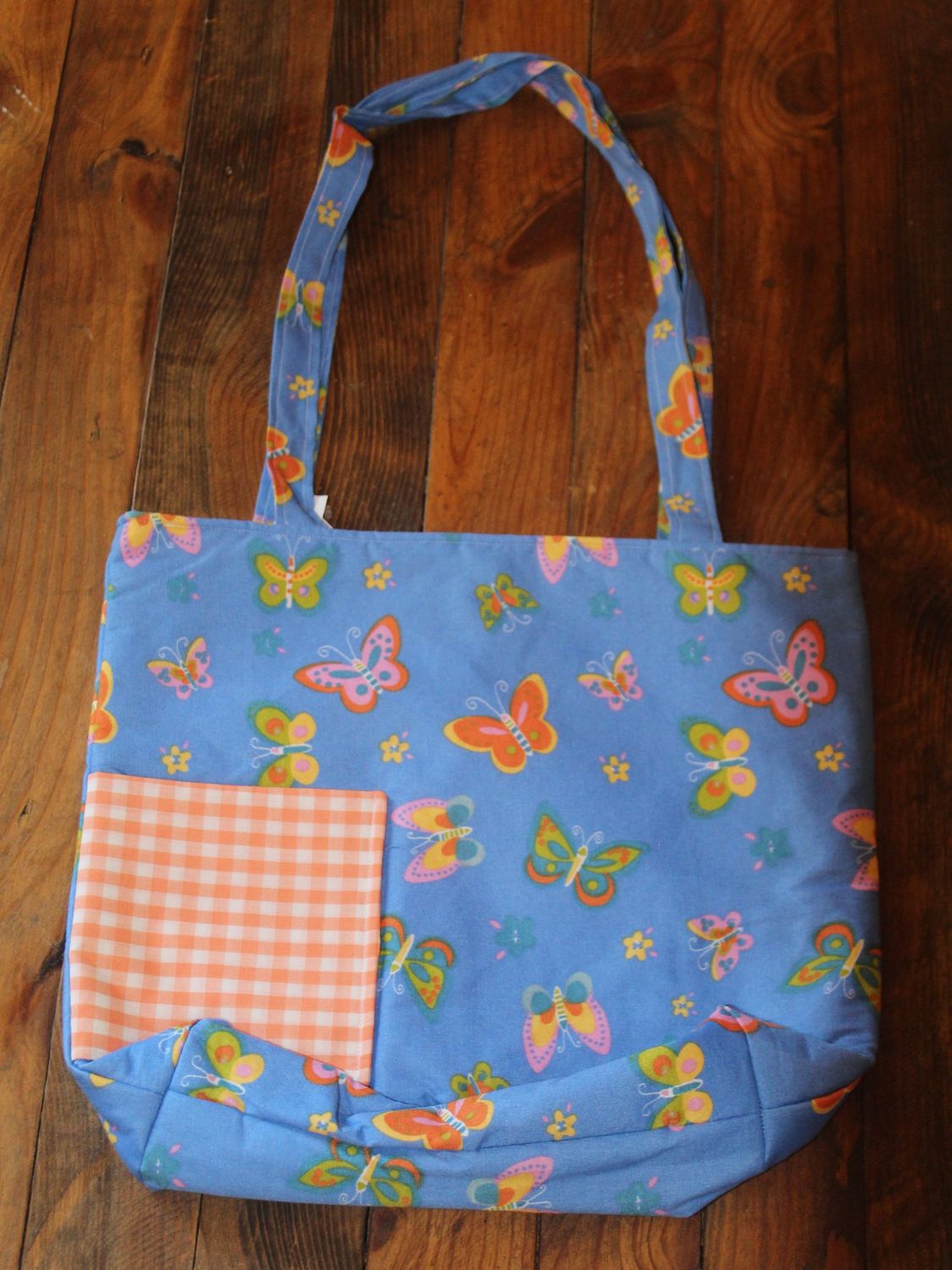 Handmade blue butterfly tote bag with orange gingham pocket on wooden background.