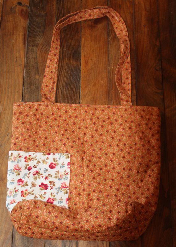 Handmade orange floral tote bag with exterior pocket on wooden background.