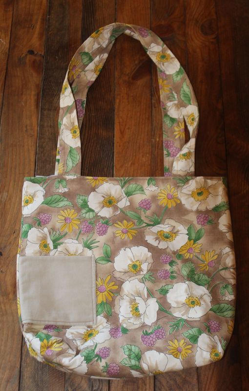 Handmade floral cotton tote bag with wildflower print and front pocket on wooden background.