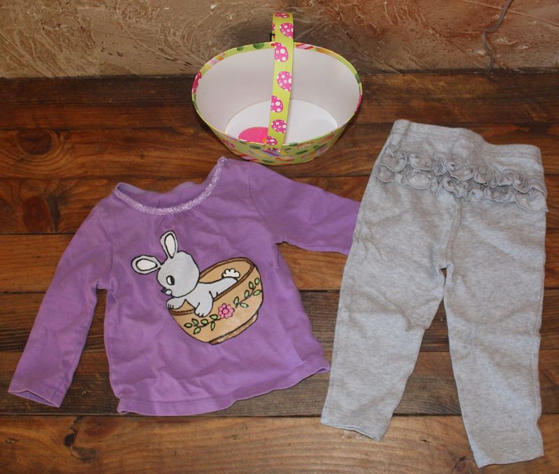 Hand painted Easter toddler girl outfit with purple bunny shirt and gray pants next to decorative Easter basket