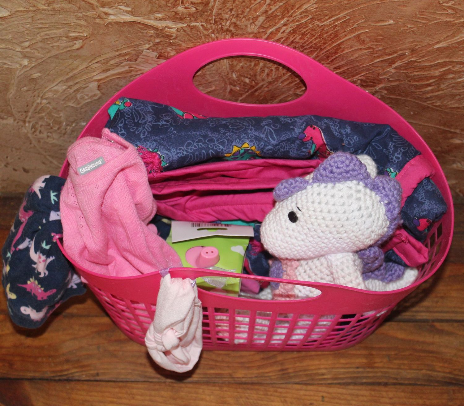 Handmade baby girl gift set with pink onesie, dinosaur leggings, crochet plush toy, and blanket in basket