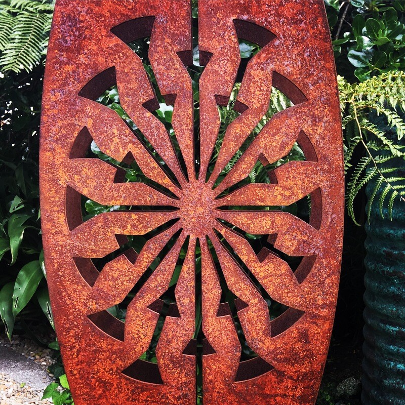 Rusty Tohu sculpture by Grounded Art NZ in a lush NZ native garden. Bold rust colour against the lush green hues of the bush.