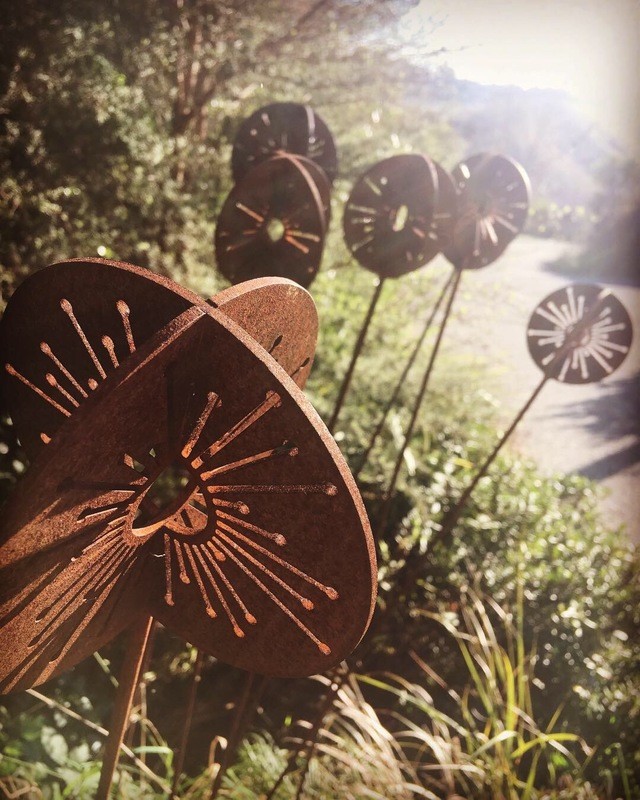 Large cluster of Corten Allium wands by Grounded Art NZ set in a Native NZ garden landscape.