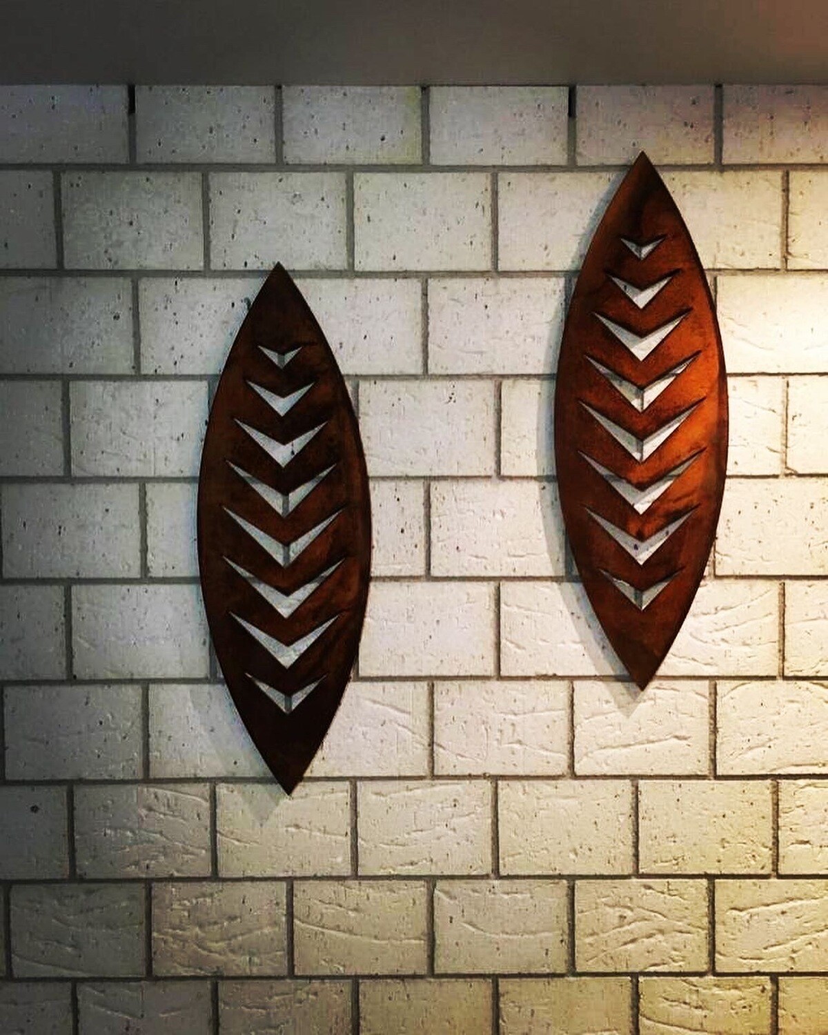 Grounded Art NZ Corten Steel Shield Wall Art in Arrow design on the exterior, natural stone cladding of a NZ home. 