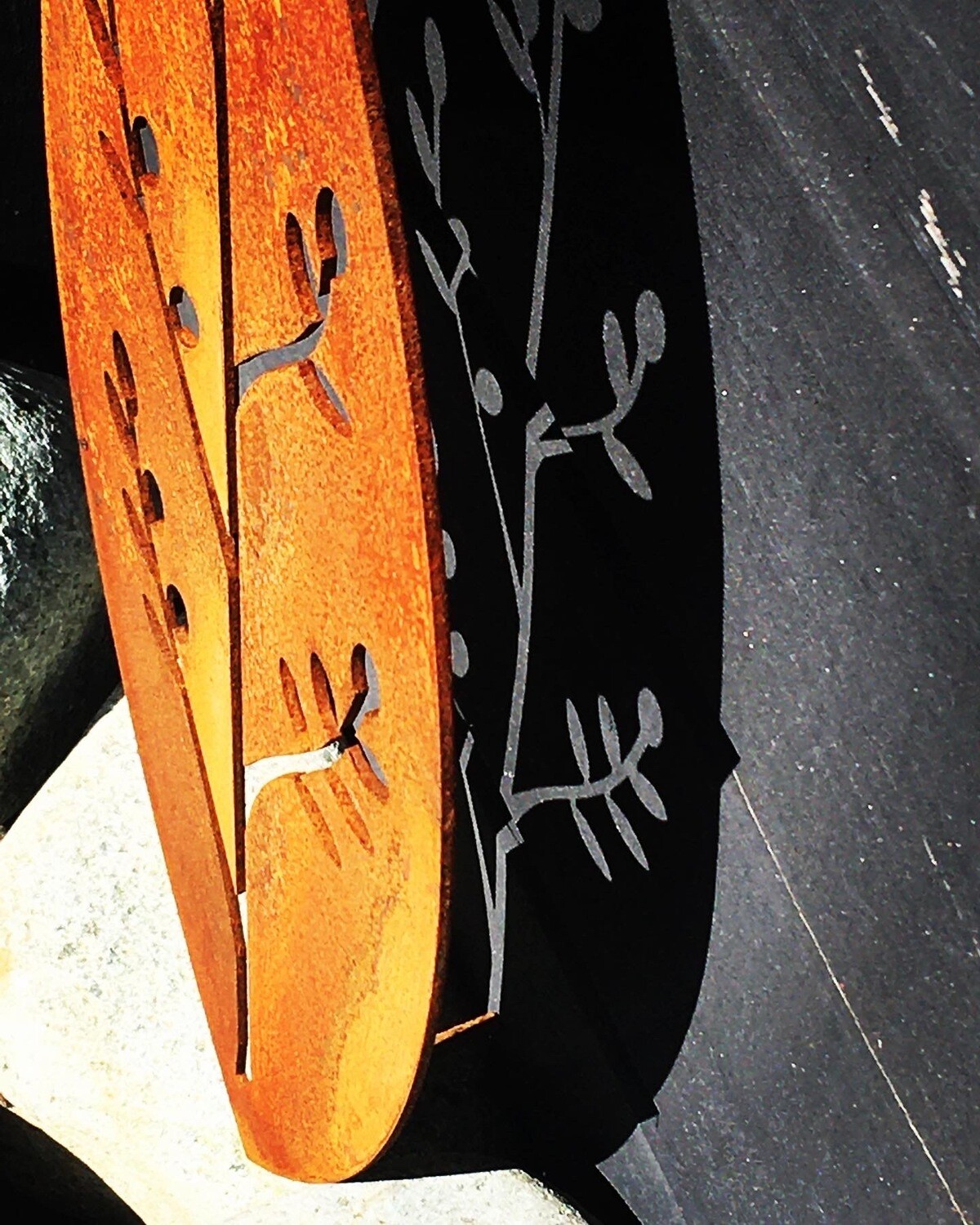 shadows created by Grounded Art NZ Corten Shield Wall Art in Korokio design. Bright rusty patina against a black wall.