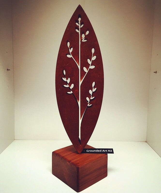 3D Corten Korokio Sculpture by Grounded Art NZ in small wooden base in a lit gallery display. NZ made rusty metal art.