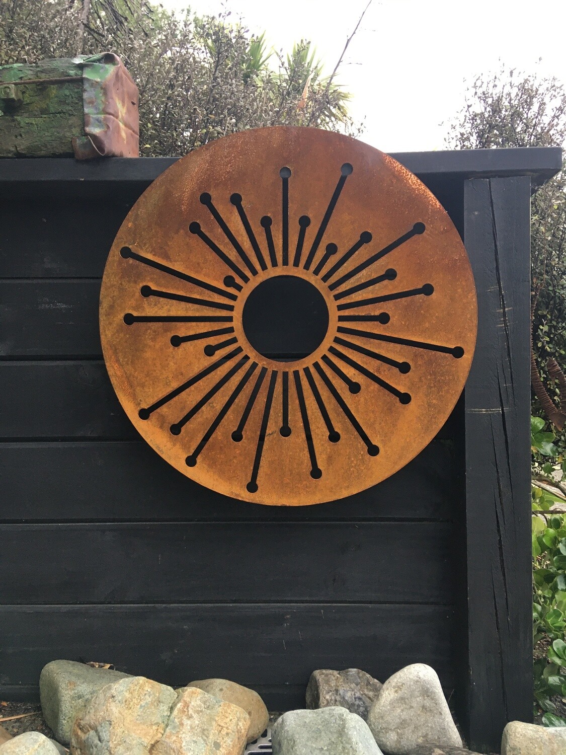 750mm Corten Allium Wall Art in bright rusty Corten Patina against a black wall. Creating contrast in an outdoor landscape. 