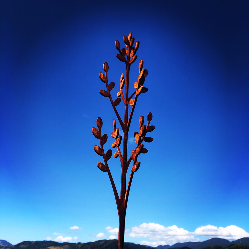 Corten Steel Toi Wands by Grounded Art NZ. Delicate wand made in a bright rusty Corten stands out infront of a deep blue sky.