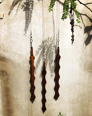 3 Corten Kowhai pods by Grounded Art NZ. Hanging infront of a natural stone wall the rusty Corten stands out in contrast.