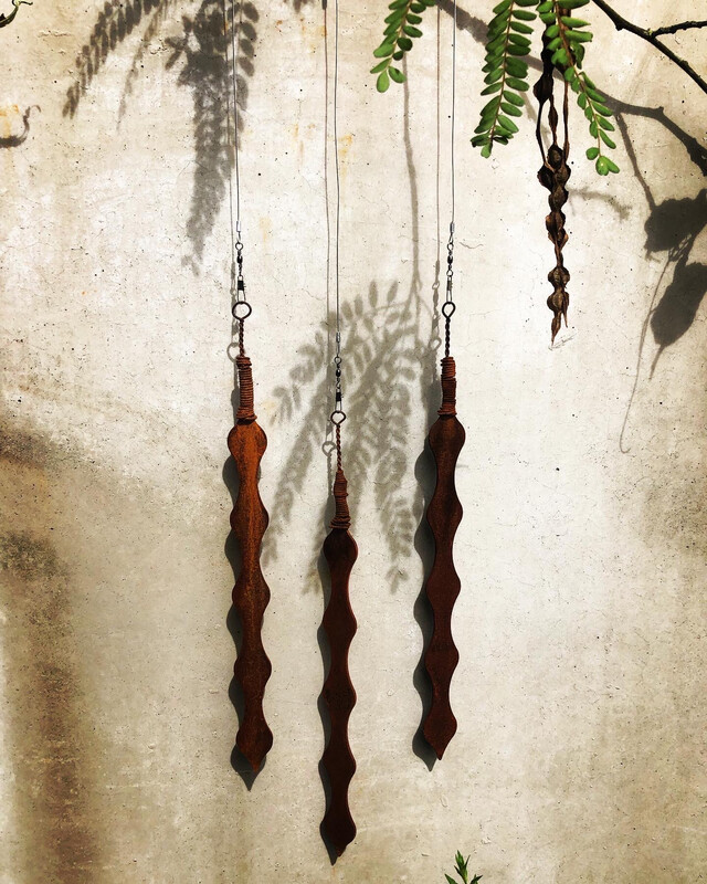 3 Corten Kowhai pods by Grounded Art NZ. Hanging infront of a natural stone wall the rusty Corten stands out in contrast.