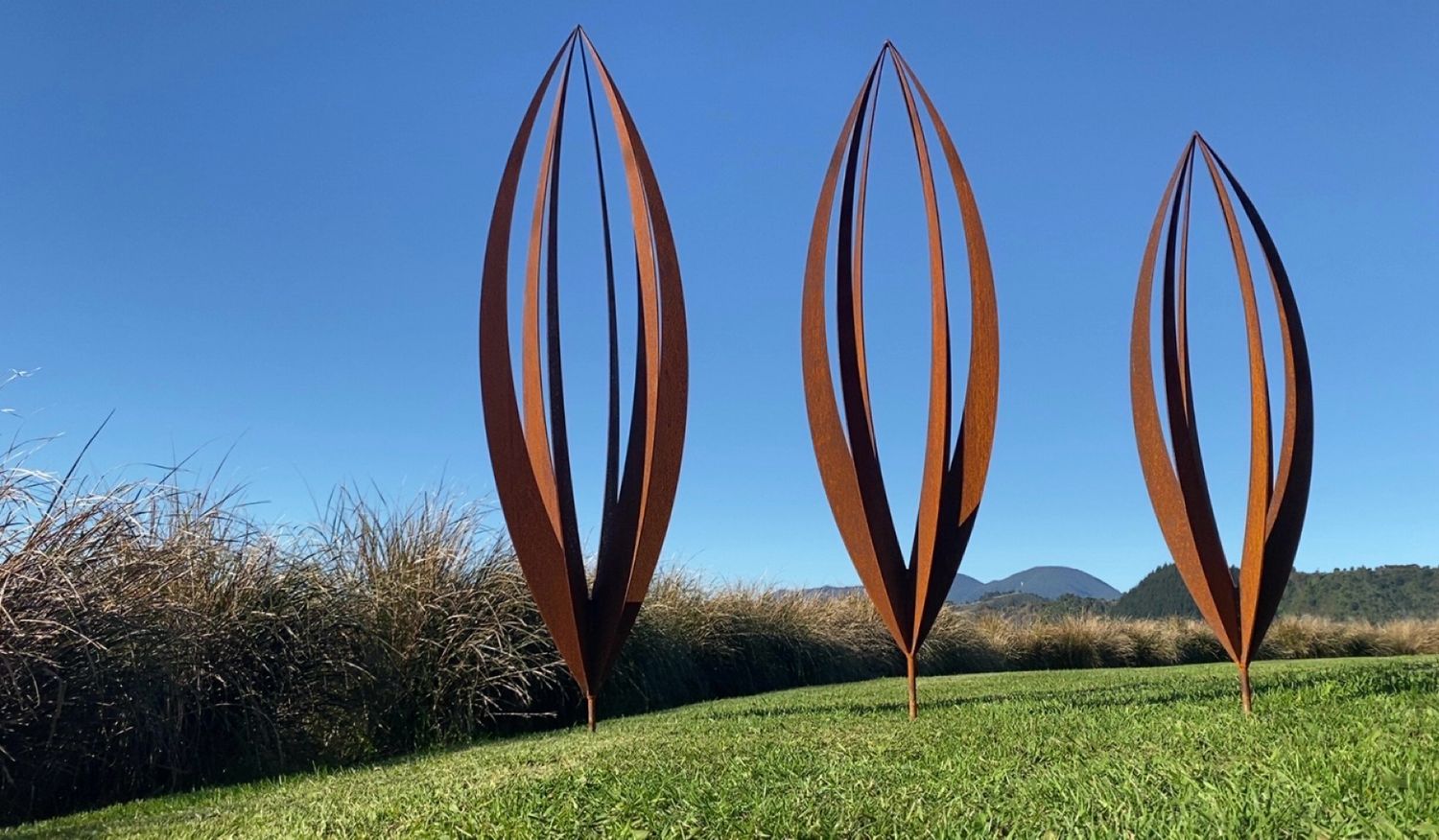 2 large Rusty Corten Pods by Grounded Art NZ on a lawn in a Native NZ garden setting.