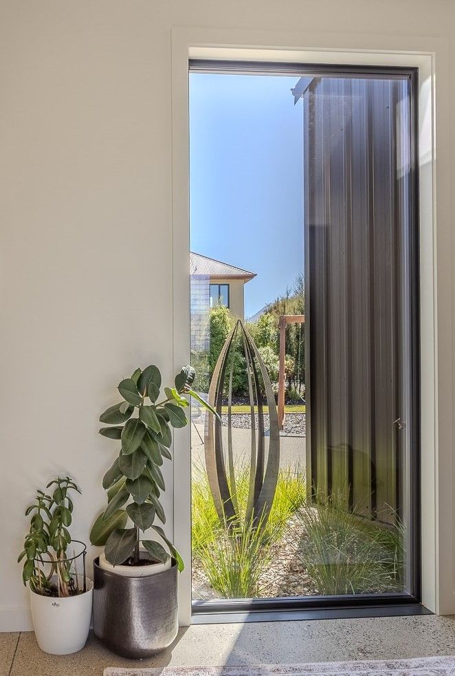 Grounded Art NZ Corten Pod before the rust has begun. framed through a tall window in a modern NZ home.