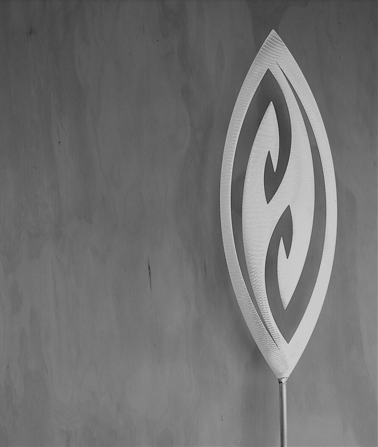 Fish Hook Aluminium Spear by Grounded Art NZ in a gallery where the shadows are cast onto the pale plywood wall behind.