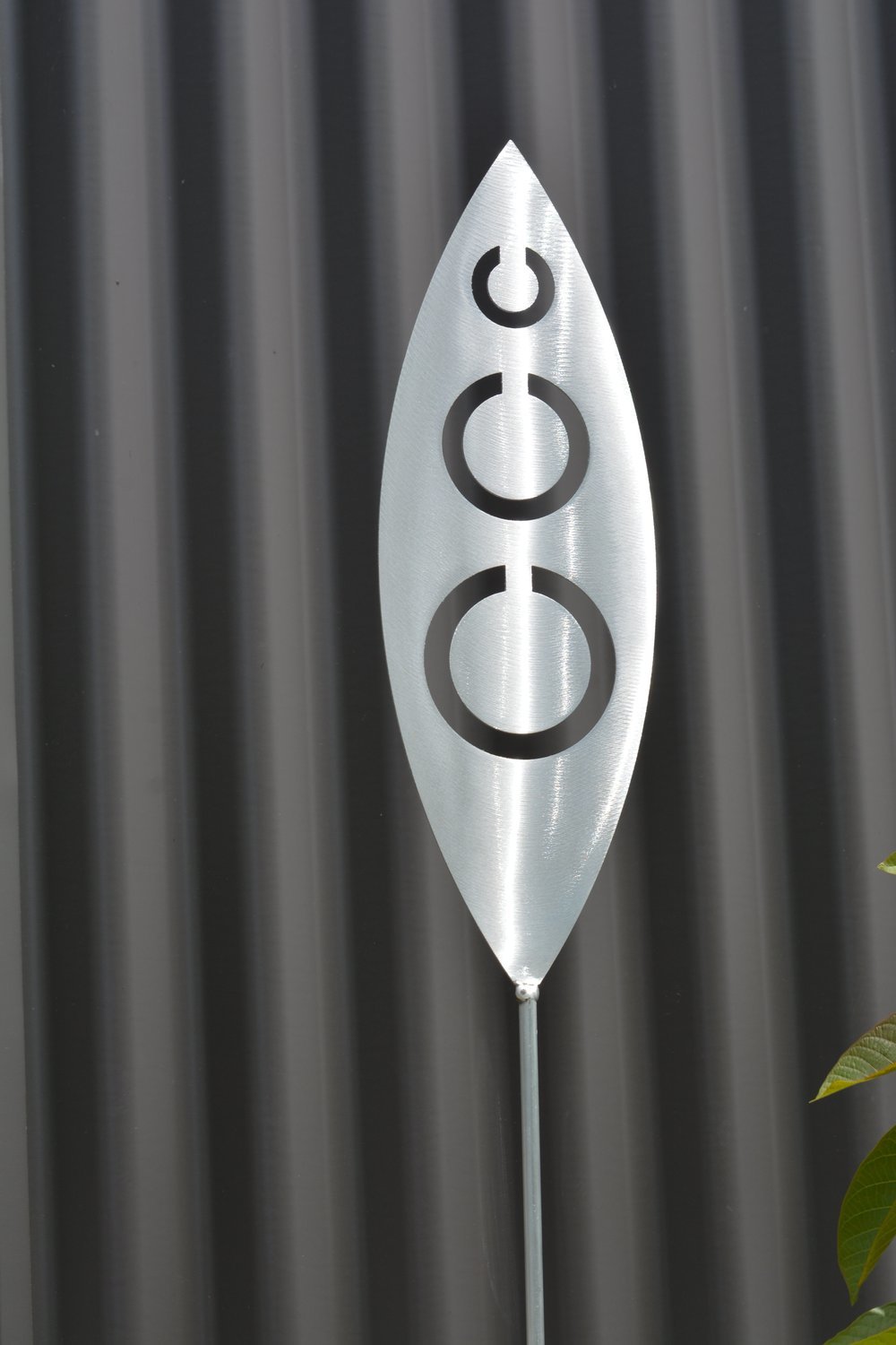Tribal Aluminium Spear by Grounded Art NZ and a dark clad building. The bright metal art pops against the dark background.