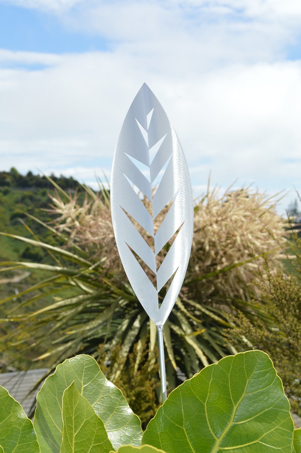 Aluminium Leaf spear by Grounded Art NZ. Glistening bright Aluminium metal art with a lush native cabbage Tree behind.