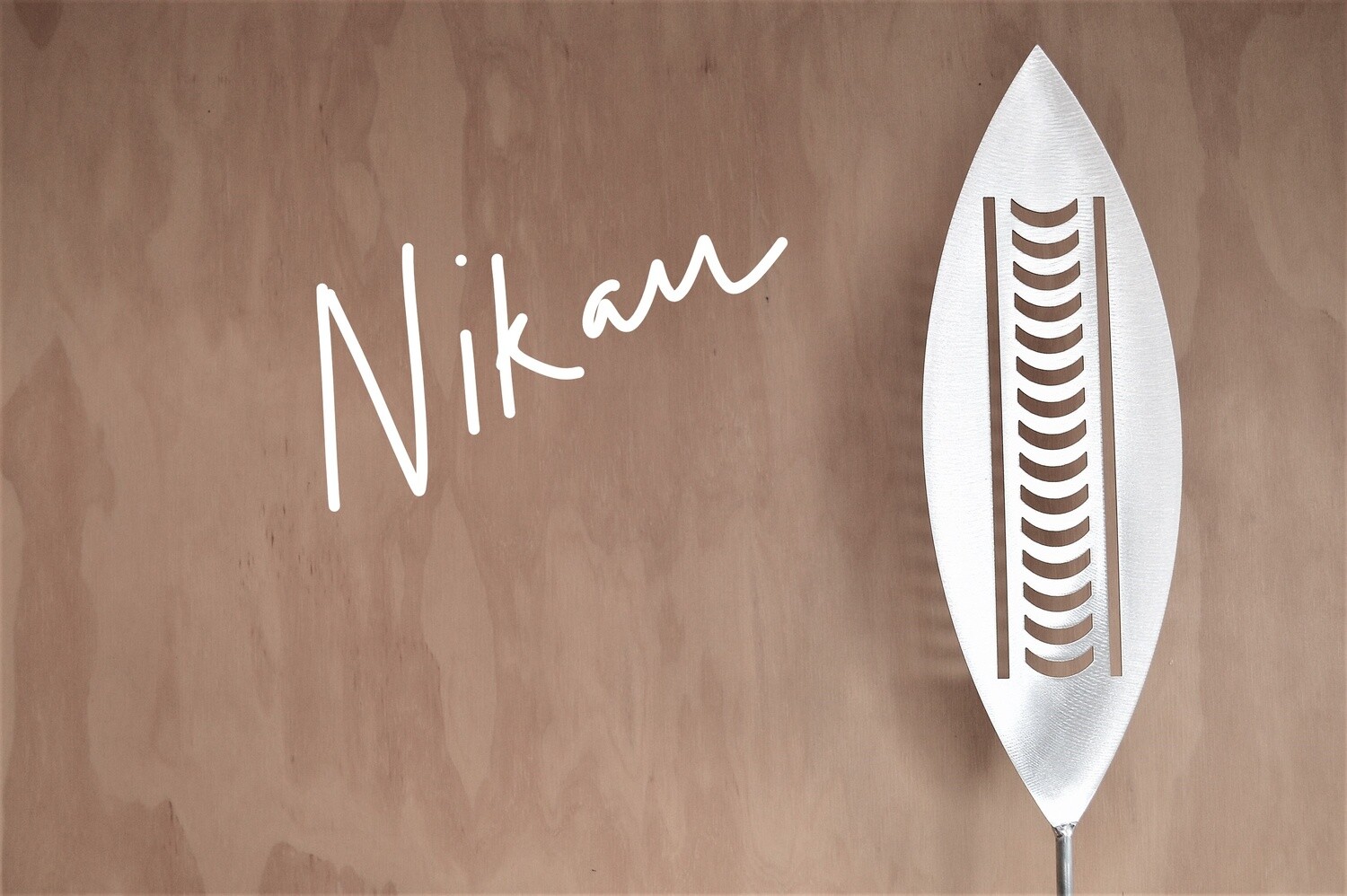 Nikau Aluminium Spear by Grounded Art NZ in a gallery setting where the shadows are cast onto the pale plywood wall behind.