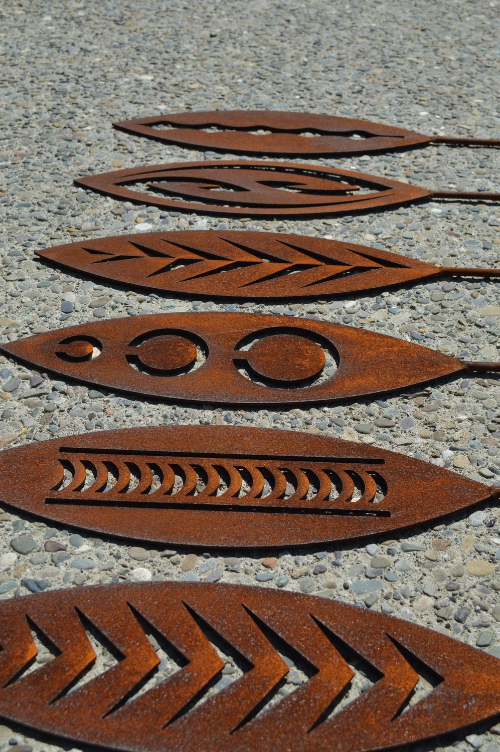 Lineup of Grounded Art NZ's rusty Corten garden spear designs laying on exposed aggregate landscaping. South Otago, NZ.