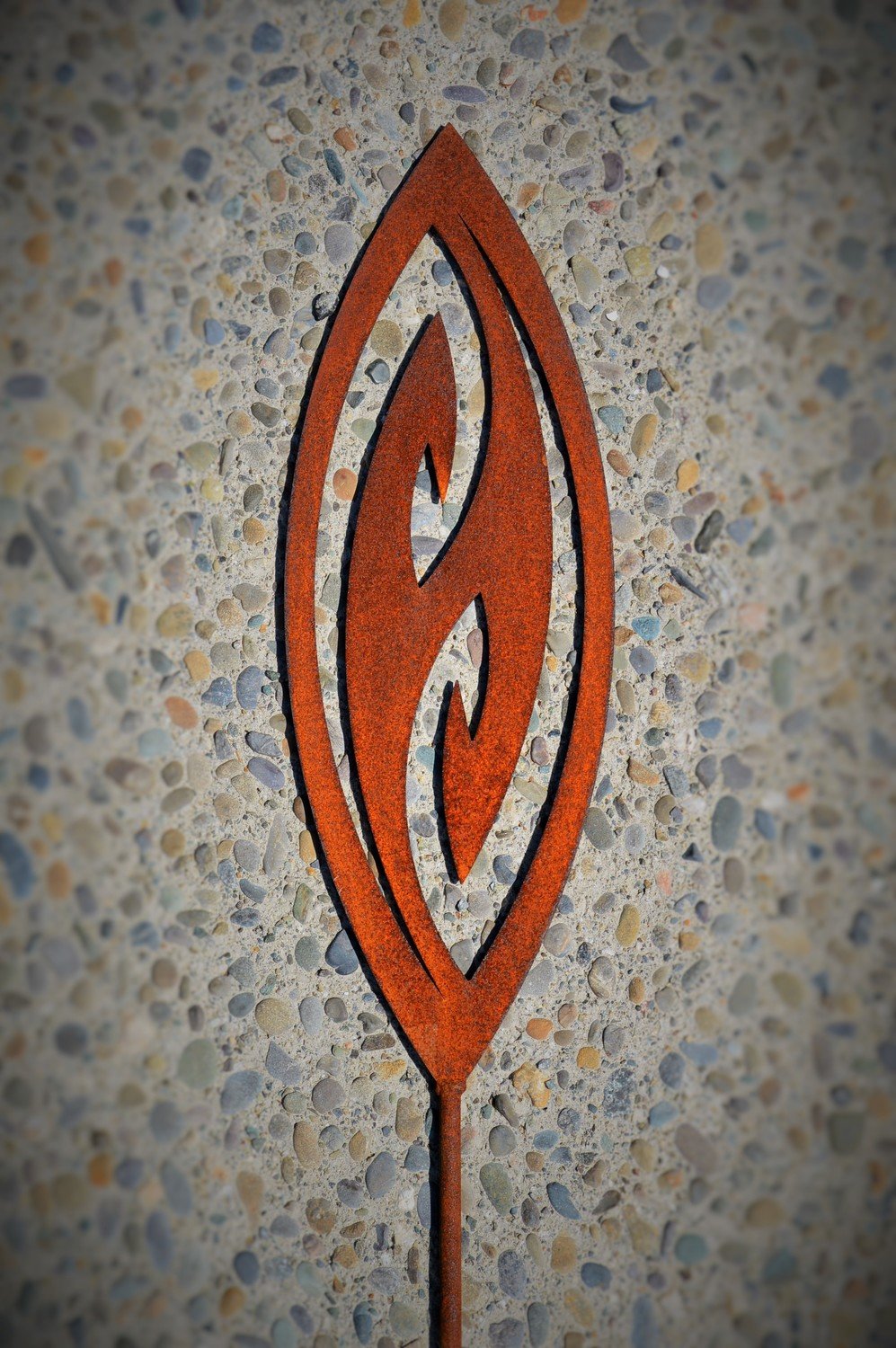 Fish Hook Corten Garden Spear by Grounded Art NZ. Its bright rusty patina contrasts against a light concrete background.