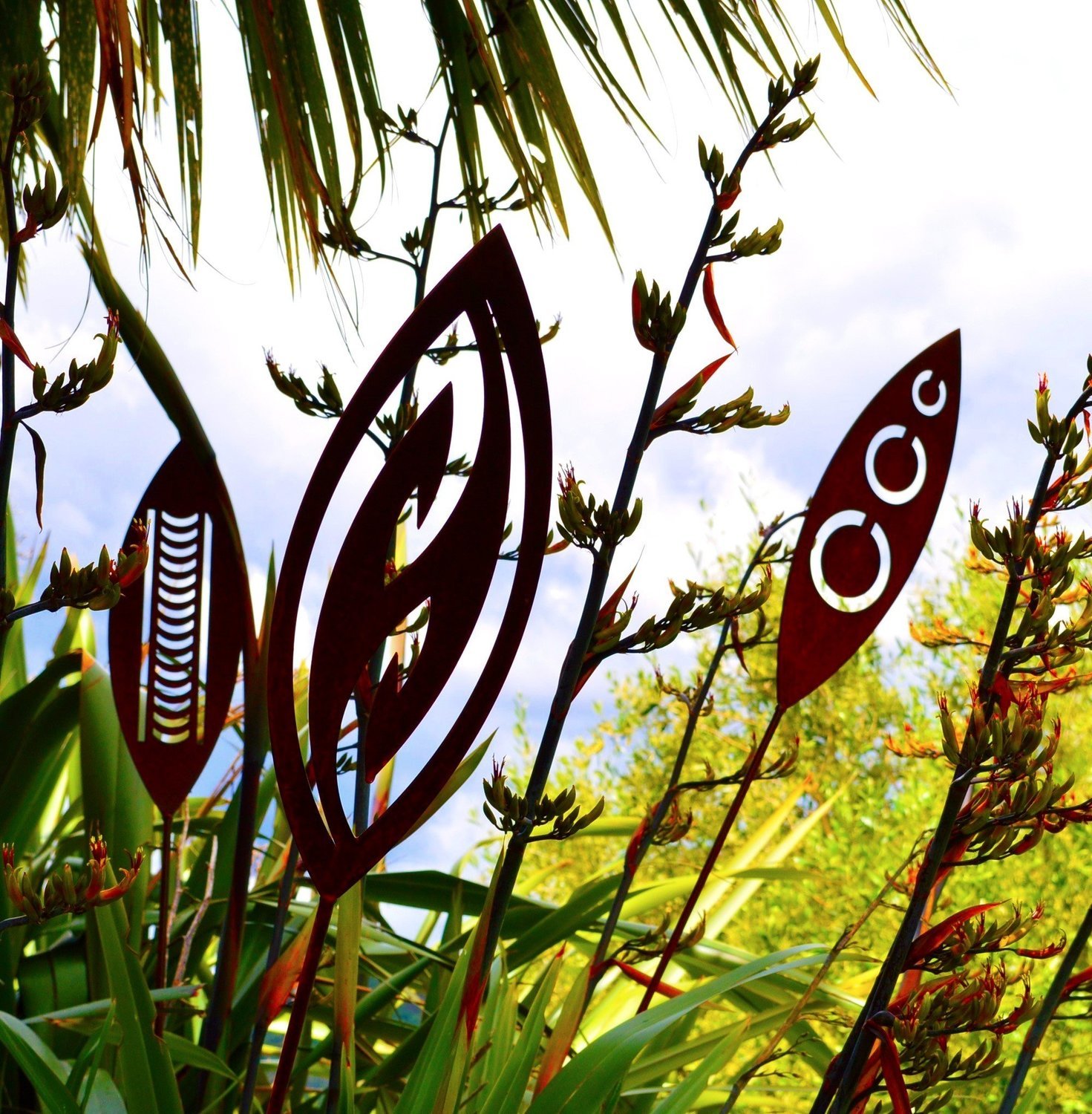 Corten Steel Spears in Nikau, Fish Hook and Tribal designs by Grounded Art NZ. Lush NZ Native plantings and landscape. 