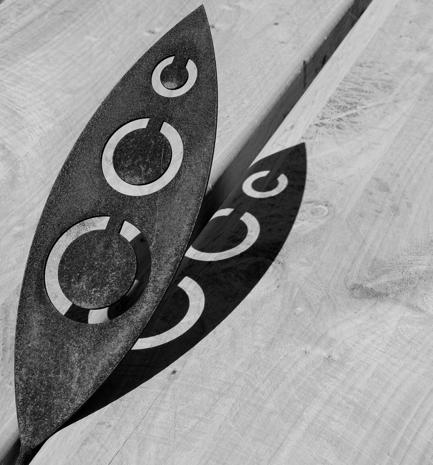 Corten spear by Grounded Art NZ in Tribal design.  Shadows cast onto a light background in contrast to the Rusty Corten.