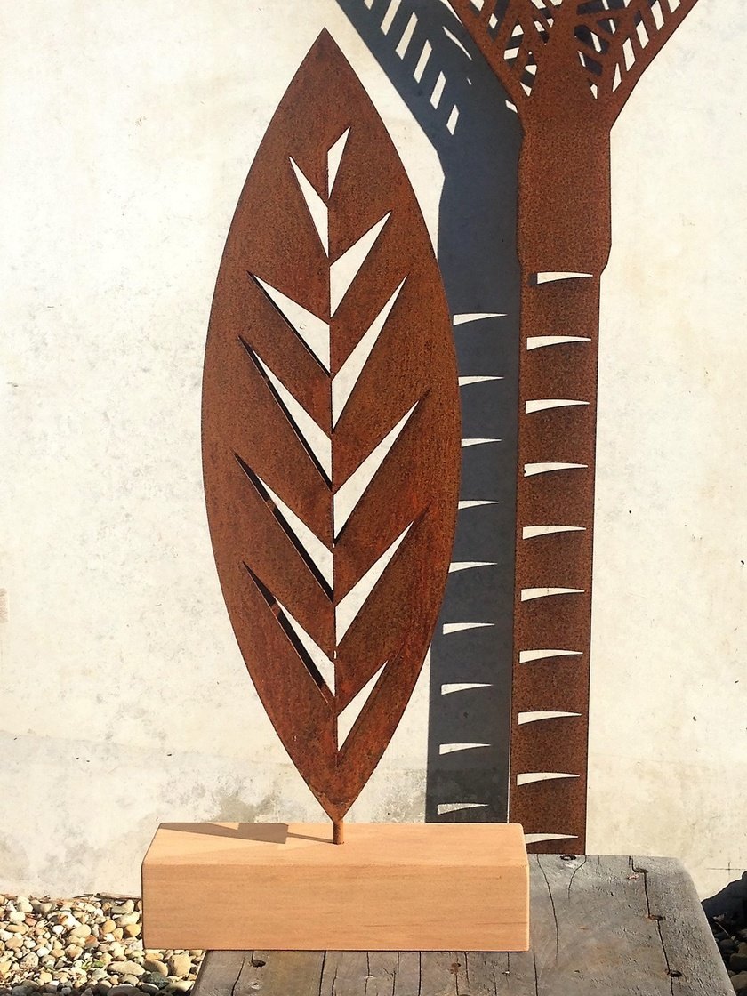 Grounded Art NZ Leaf design in rusty Corten steel displayed in front of a rusty Nikau Palm trunk against light natural stone.