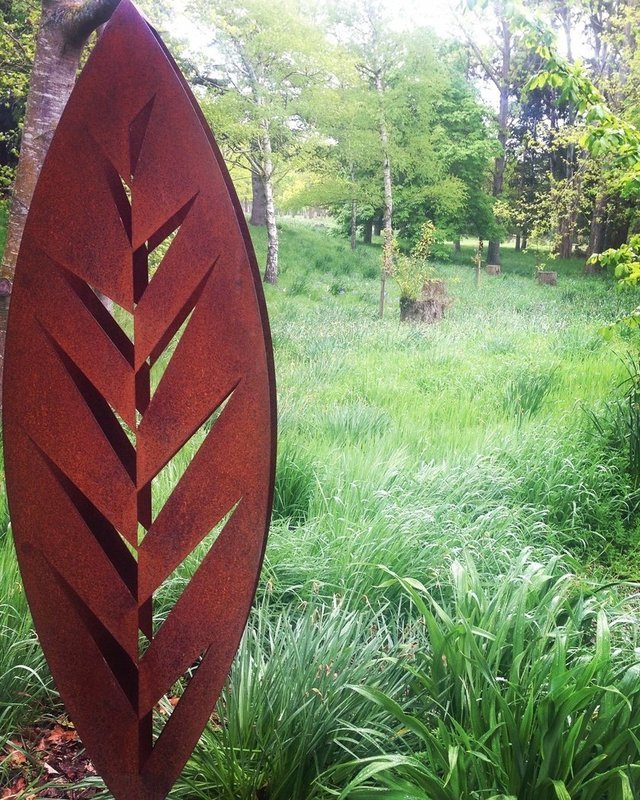 Rusty Metal 3D Corten leaf sculpture by Grounded Art NZ displayed in a lush woodland garden in Aotearoa. 