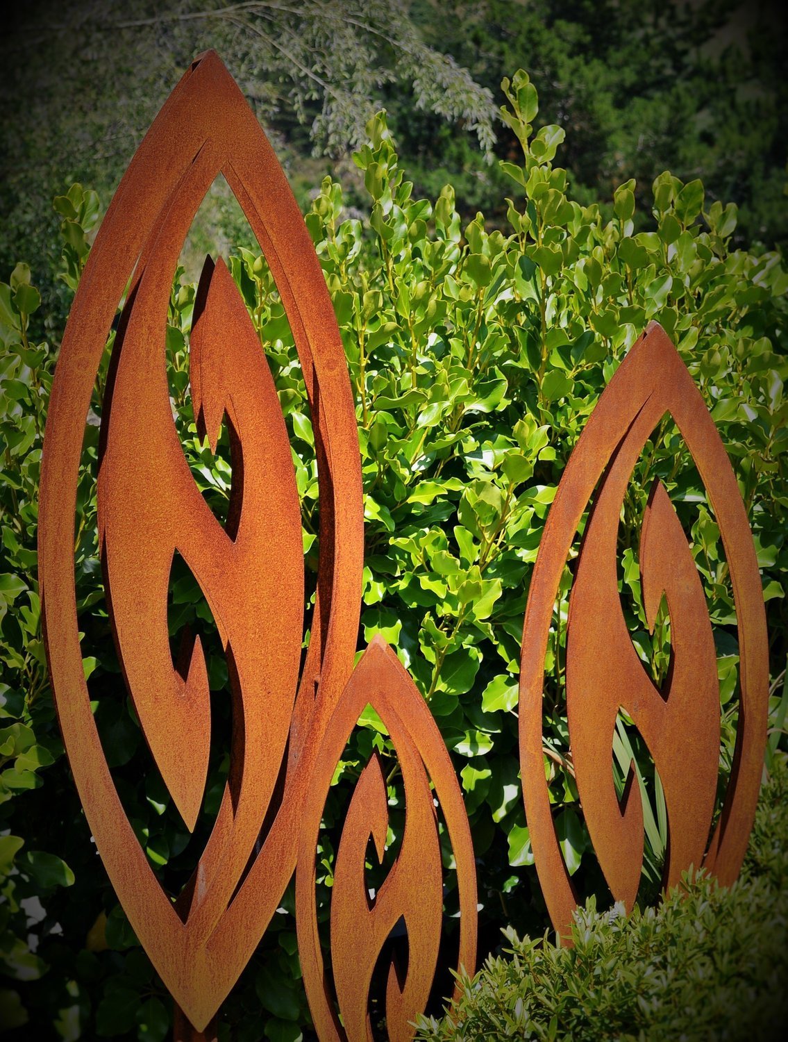 a Trio of rusty Corten Fish Hook Sculptures in a lush native NZ garden. Grounded Art NZ's signature and most popular design. 