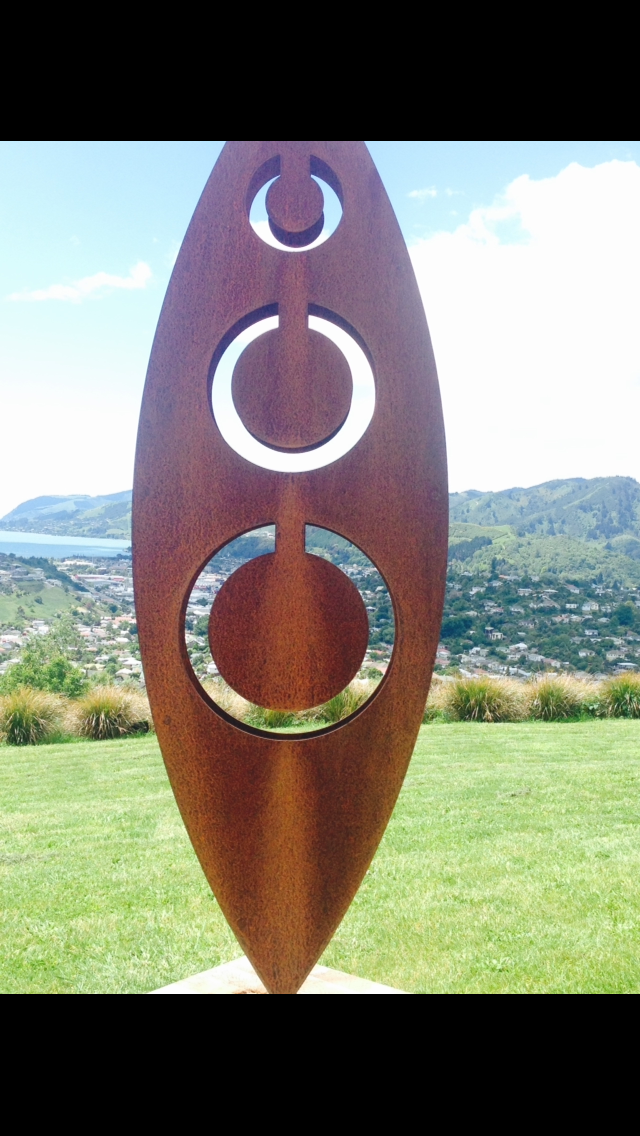 Rusty metal art in Grounded Art NZ Tribal design. 3D Garden Art located in front of a city view and native grasses and lawn.