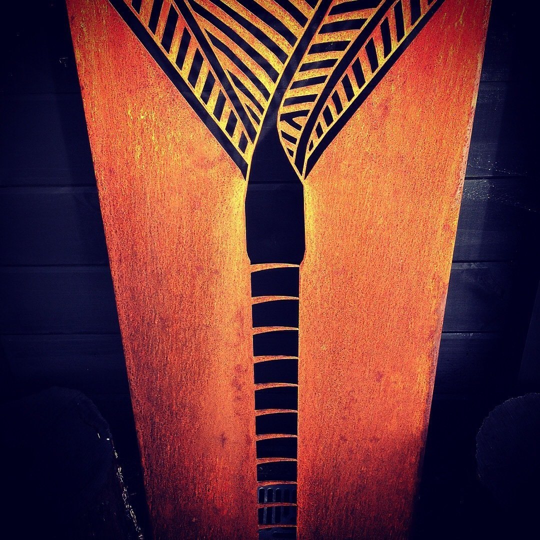 Corten Nikau panel by Grounded Art NZ against a black wall. Bright Patina is highlighted by the dark background.