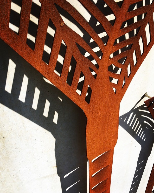Corten Nikau Palm Wall Art by Grounded Art NZ. Bright rusty patina stepped out from stone wall throwing shadows of the Nikau.