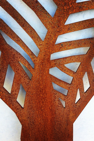 Close up of a Corten Nikau Palm Wall Art by Grounded Art NZ. Bright rusty Corten patina against a pale natural stone wall.