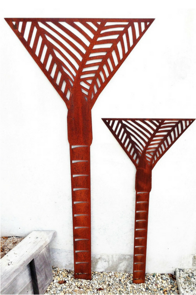 2 Corten Nikau Palm Wall Art by Grounded Art NZ. Bright rusty patina against a light stone wall.