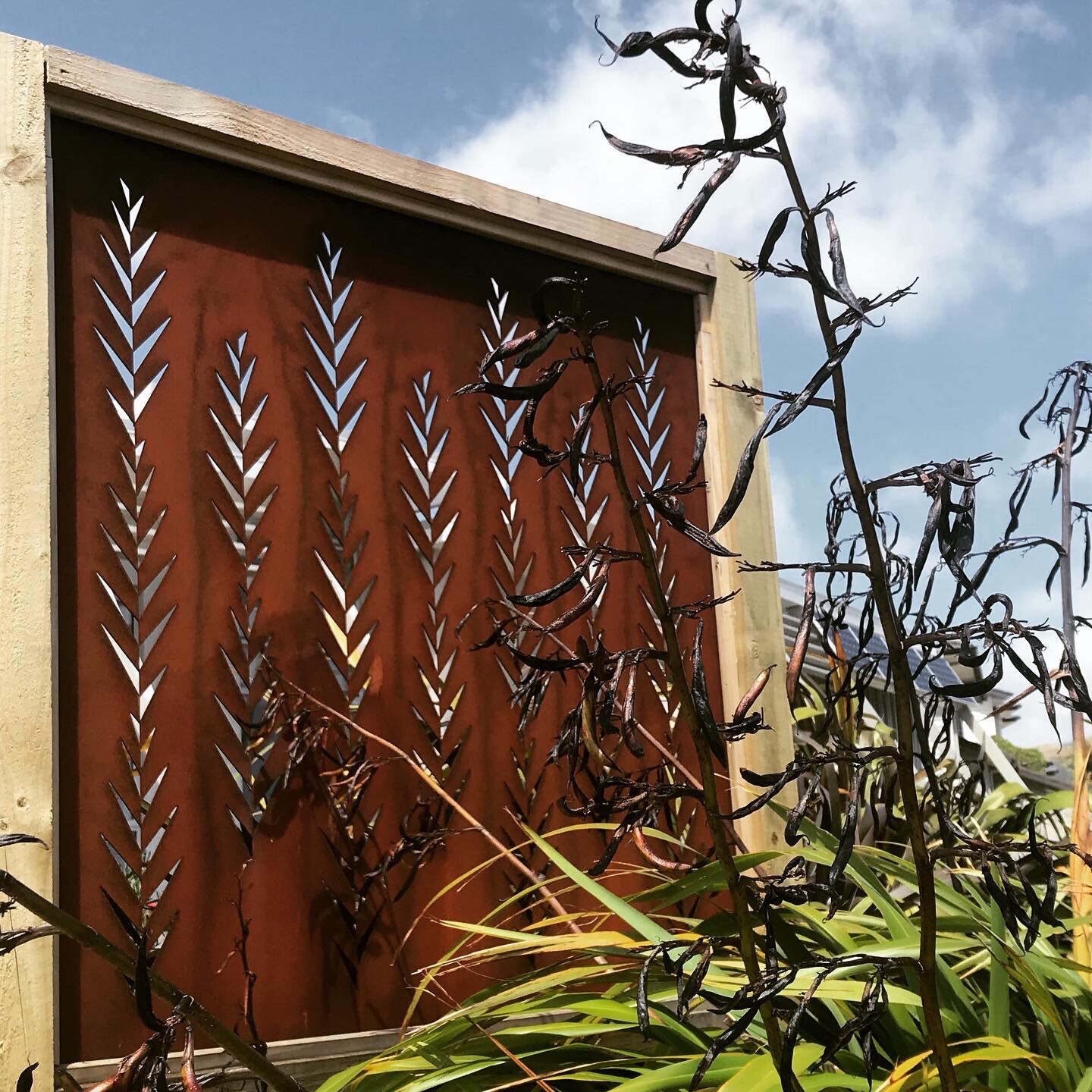 A Grounded Art NZ Rusty Corten Leaf Screen in a wooden frame located in amongst Native NZ Flax pods and leaves. 