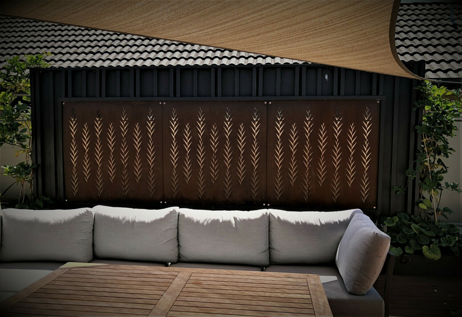 Outdoor seating area given privacy from a series of Grounded Art NZ Leaf Screens along a boundary fence with a shade sail.