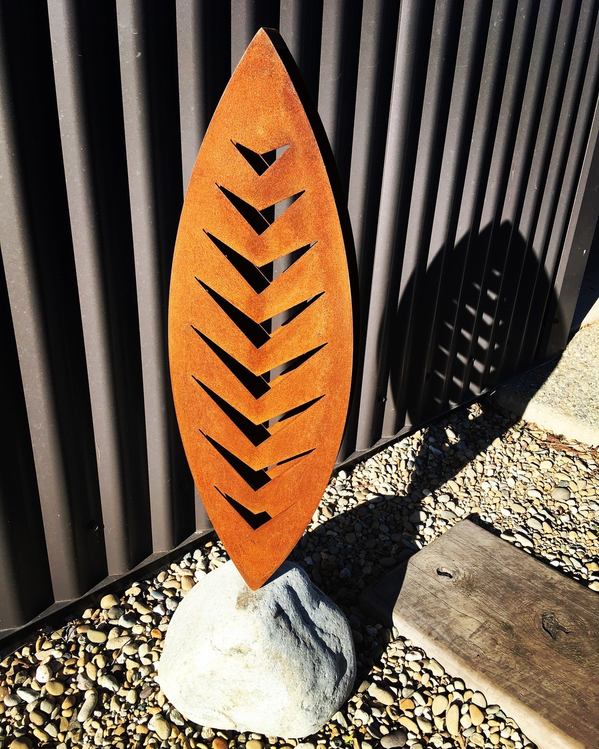 3D Rusty Arrow Corten sculpture by Grounded Art NZ in a natural stone base with dark iron cladding behind.