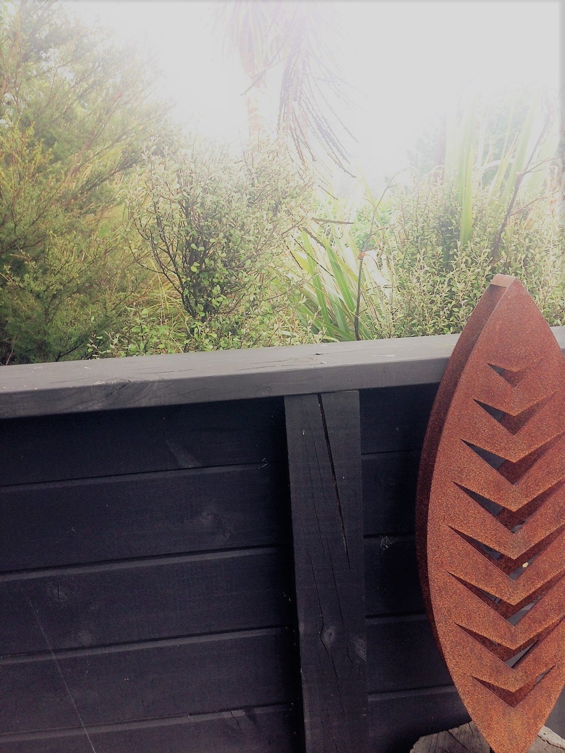 3D Corten Arrow Sculpture by Grounded Art NZ. Warm weathered steel against the dark wall and lush native NZ garden.