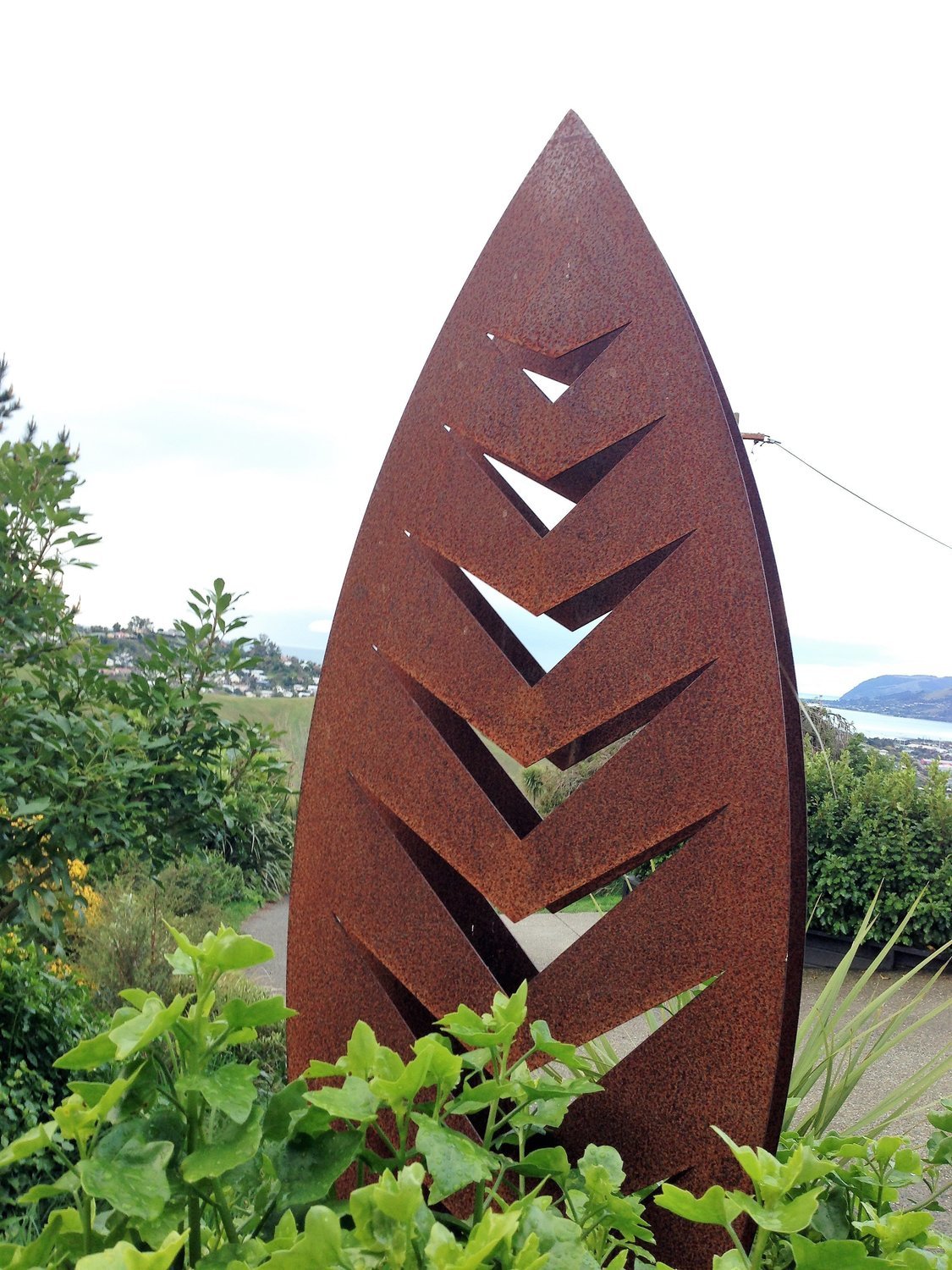 3D Corten Arrow Sculpture by Grounded Art NZ. Warm weathered steel against the lush native NZ garden.