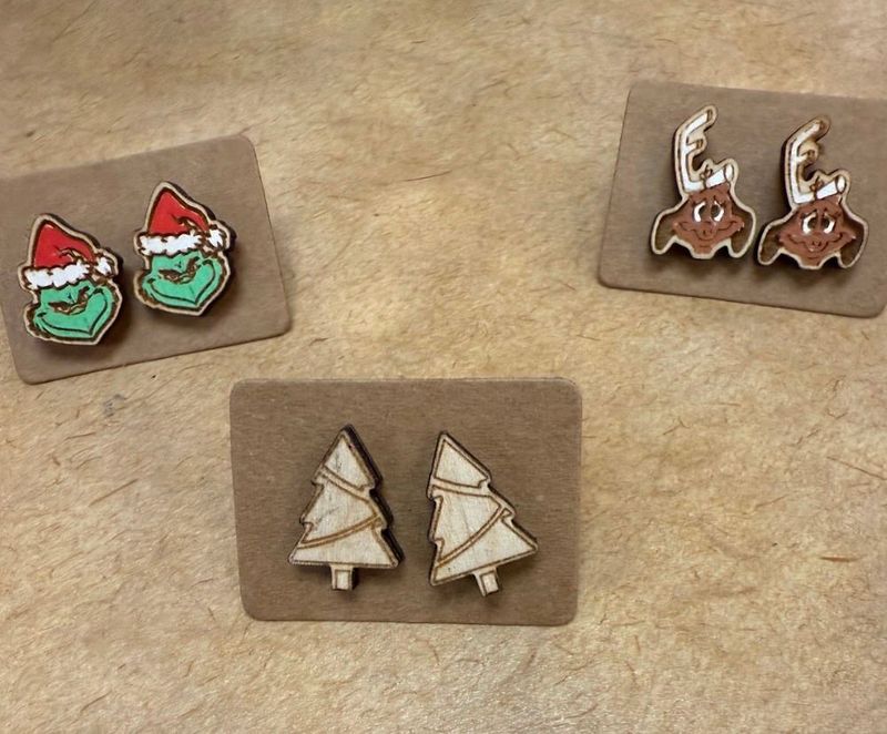 Holiday Earrings | Grinch, Max the Dog, & Christmas Trees laid out on a counter at Merle Norman Elizabethton. 
