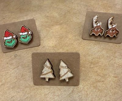 Holiday Earrings | Grinch, Max the Dog, & Christmas Trees laid out on a counter at Merle Norman Elizabethton. 