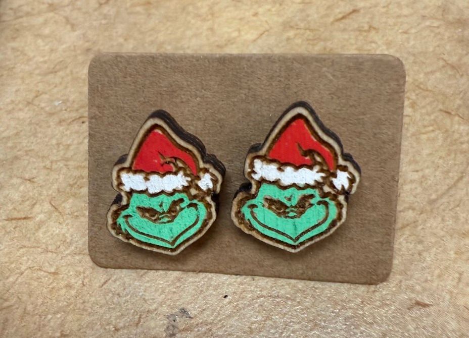 Holiday Earrings | Grinch, Max the Dog, & Christmas Trees laid out on a counter at Merle Norman Elizabethton. 
