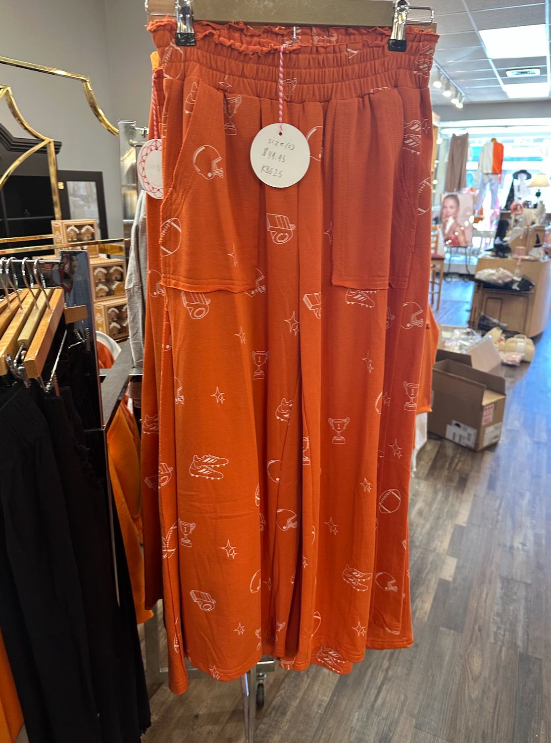 Ladies Orange Football Flowy Pants hanging on a rack in Merle Norman Elizabethton. 