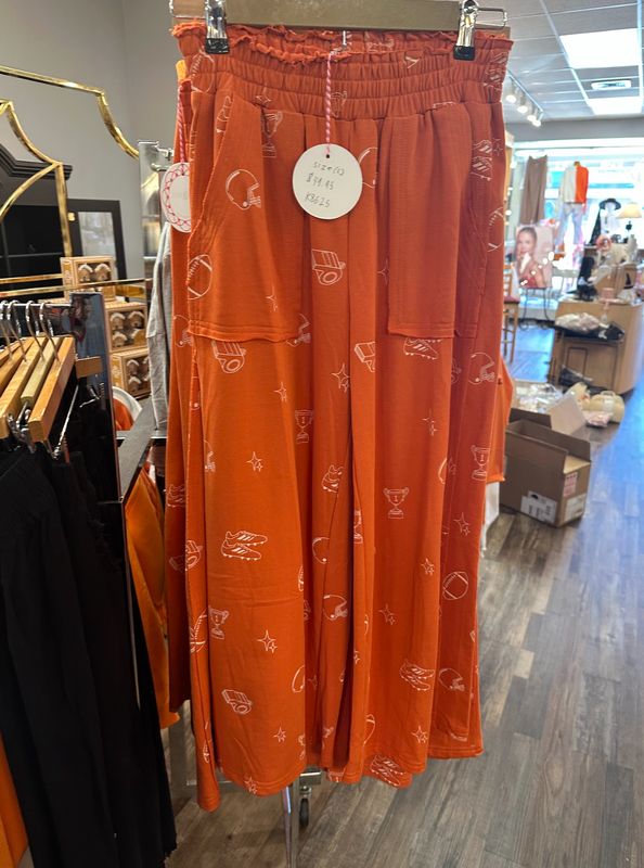 Ladies Orange Football Flowy Pants hanging on a rack in Merle Norman Elizabethton. 