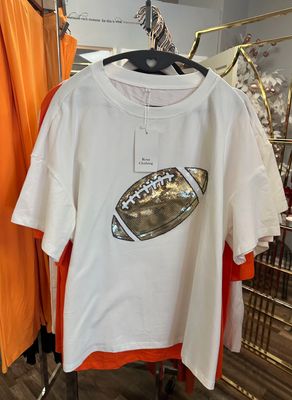 Rosa Clothing Football  T-shirt in White & Shimmering gold hanging on a rack in Merle Norman Elizabethton. 
