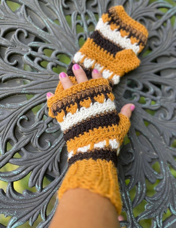 Hand-Crocheted Alpaca Fingerless Gloves - Mustard, Brown & White Hand-crocheted alpaca fingerless gloves in mustard gold, brown, and white, with one glove worn and the one resting on a table