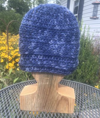 Denim blue hand-crocheted alpaca hat with textured stitches and subtle lighter blue accents, displayed on a wooden hat stand 
